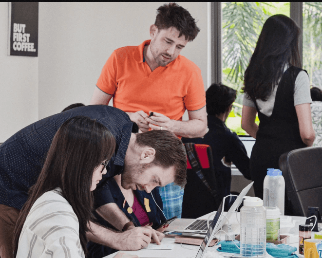 Group of people collaborating at a table with laptops and documents in a bright, modern office setting.